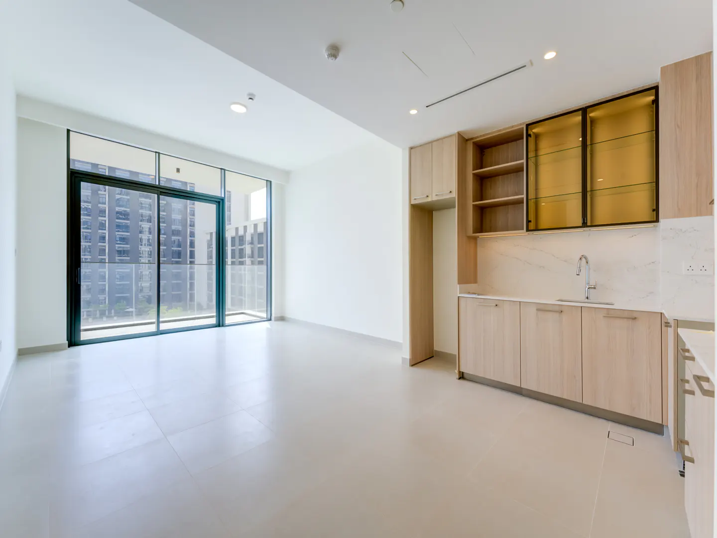 Bright, empty apartment with light wood cabinets, marble countertops, and a large sliding glass door to a balcony.