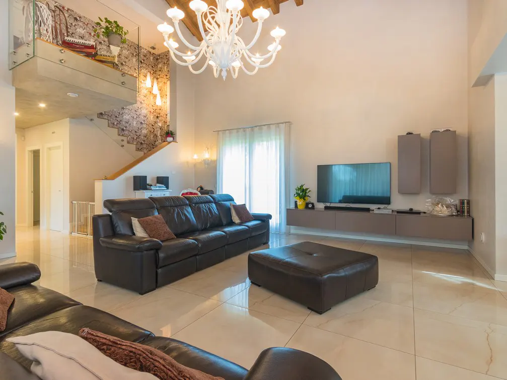 A bright living room with a brown leather sofa, ottoman, TV, and a white chandelier.