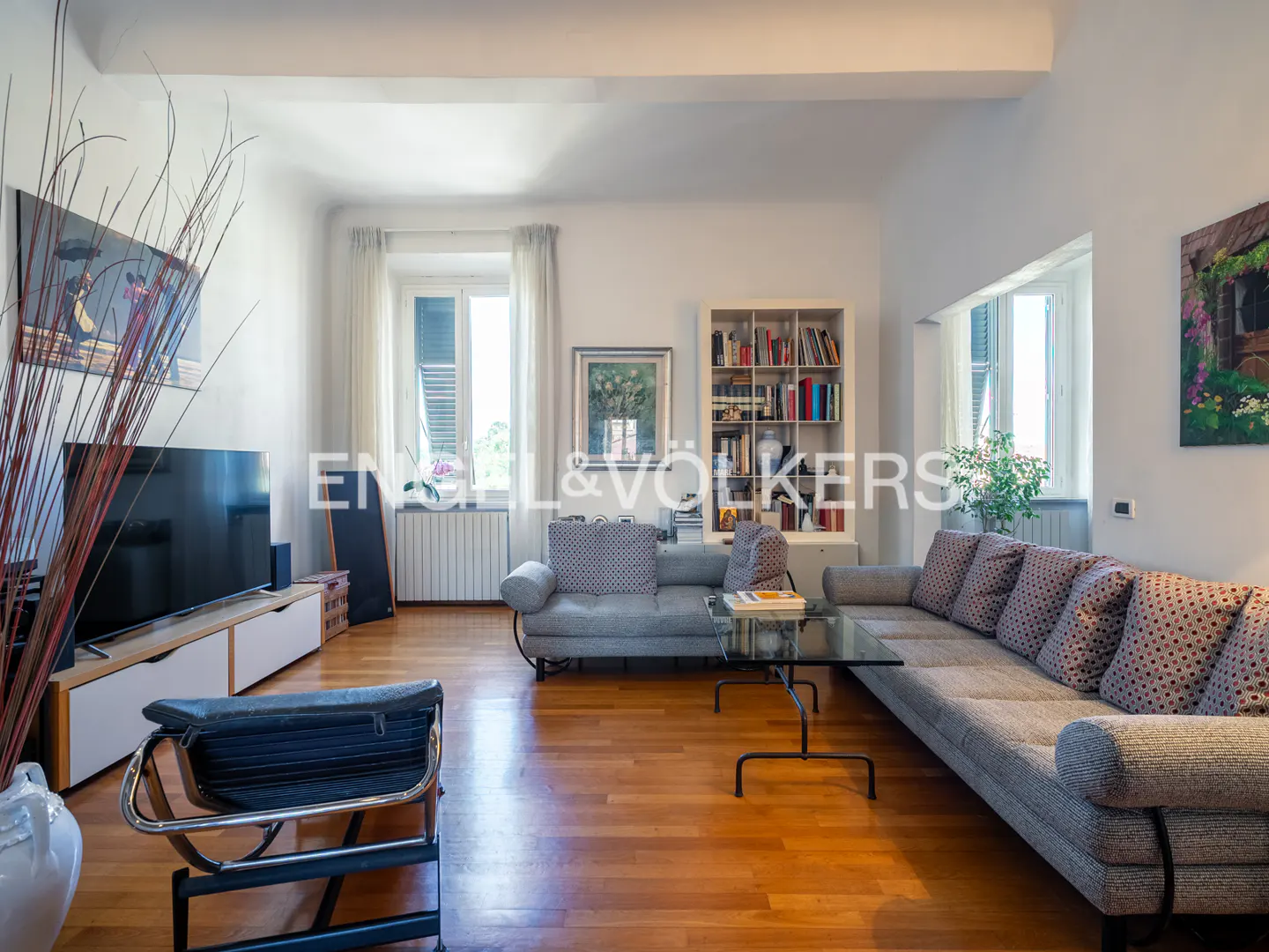 Bright living room with hardwood floors, a gray sectional sofa, a glass coffee table, and a TV on a white media console.