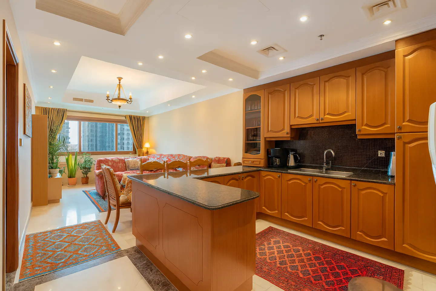 Open-concept living space with wood cabinets, island, and floral sofa. A chandelier hangs above the living area.