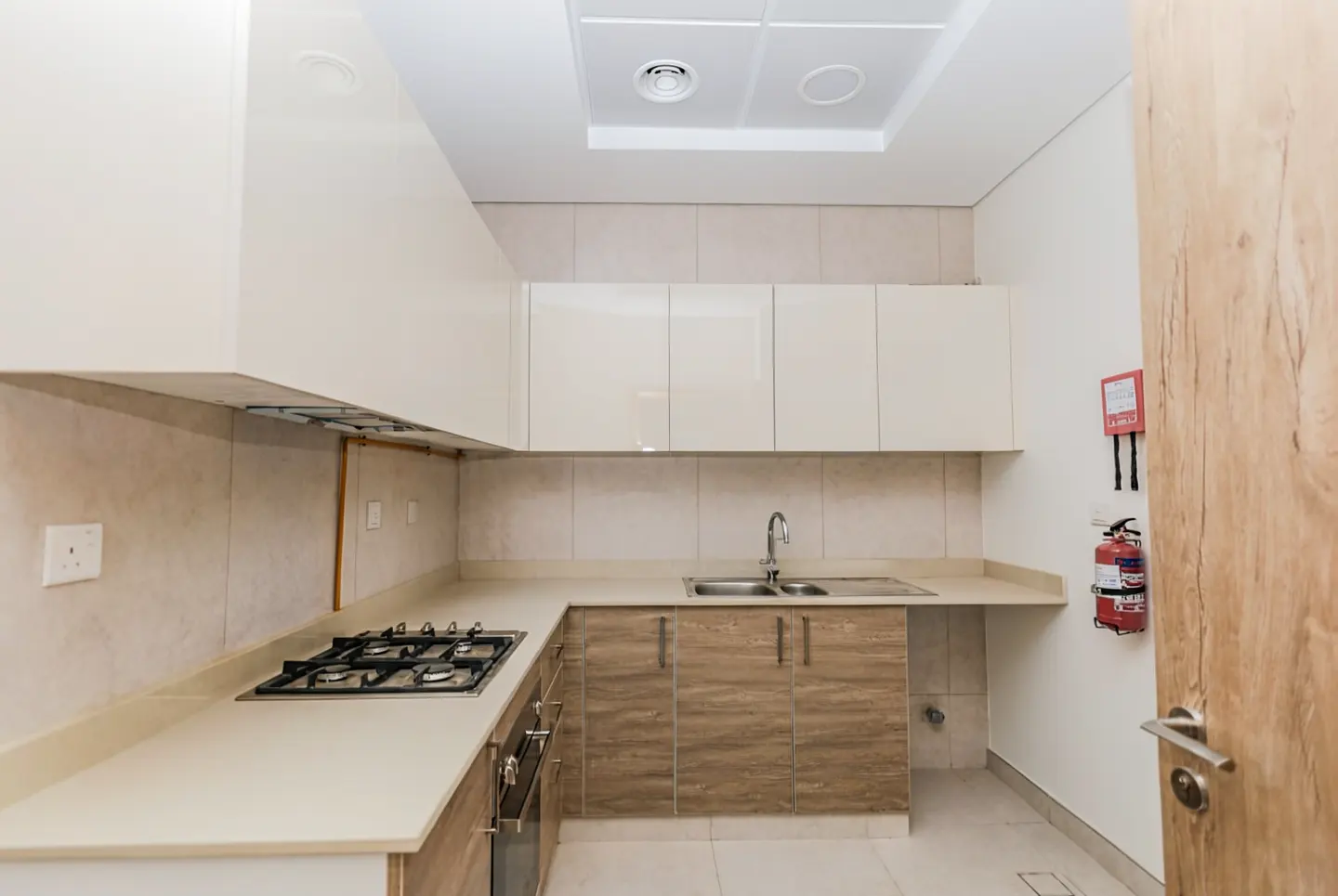 Bright kitchen with white cabinets, stone countertops, and a gas stove. A fire extinguisher hangs near a wood-grain door.