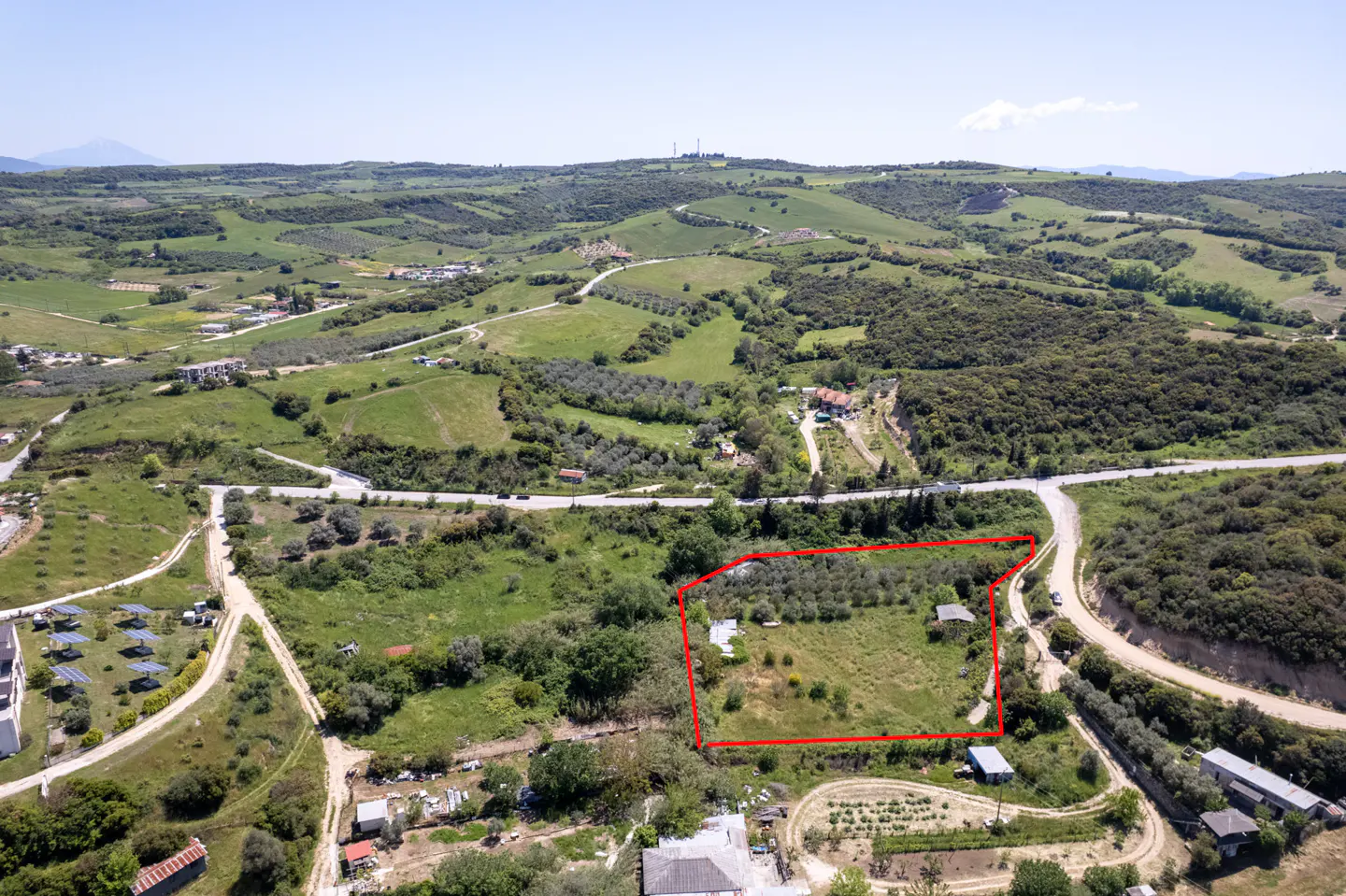 Aerial view of a green, rural landscape with a property outlined in red. Rolling hills and scattered buildings are visible.