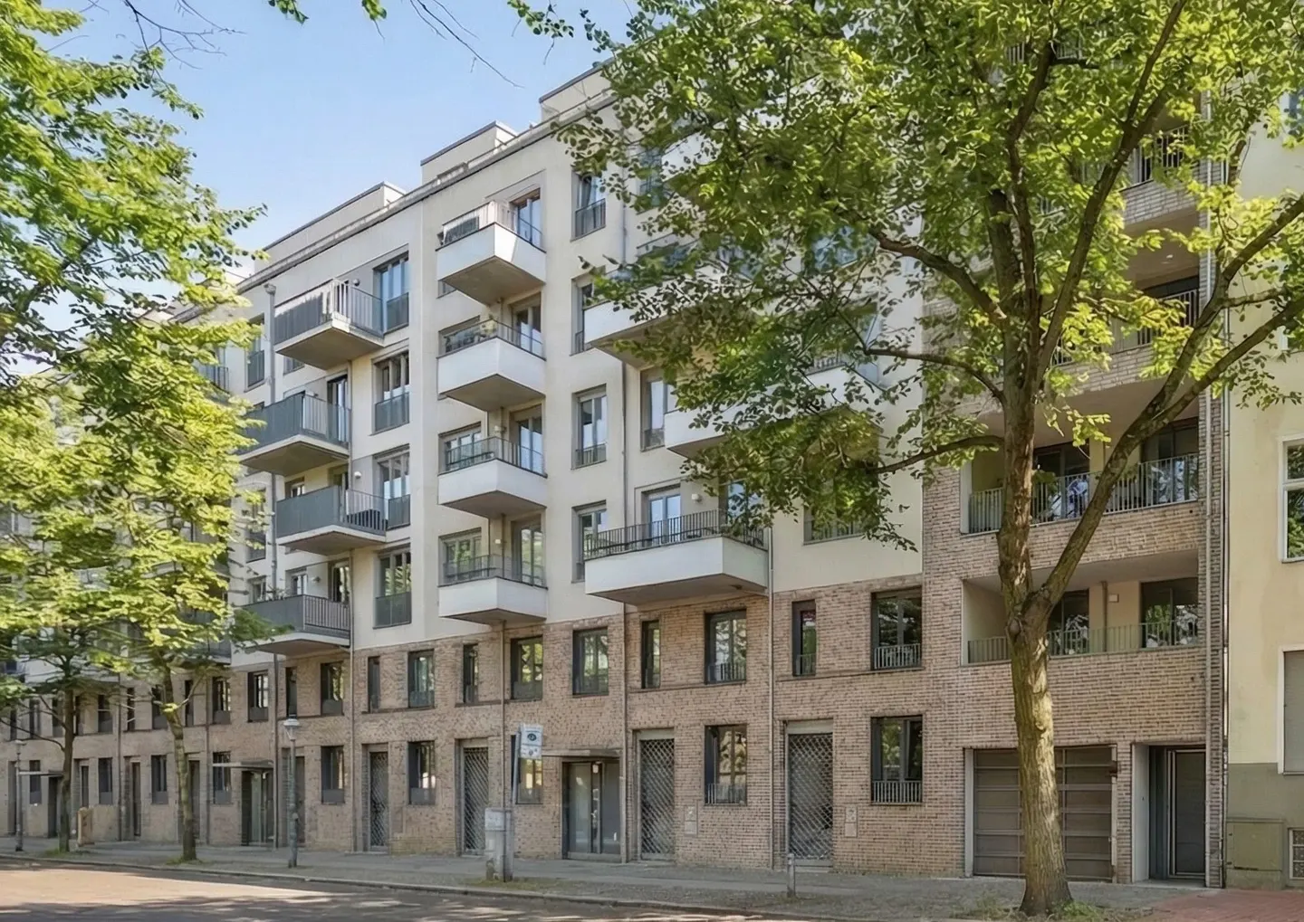 Modern apartment building with balconies, a brick facade, and green trees on a sunny day.