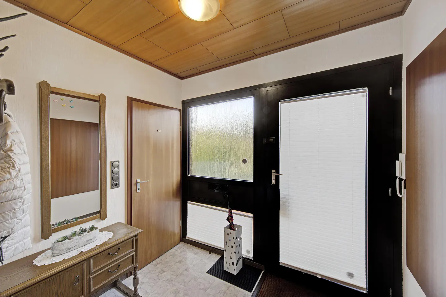 A home's entryway with a wooden ceiling, a mirror, and a black-framed glass door.