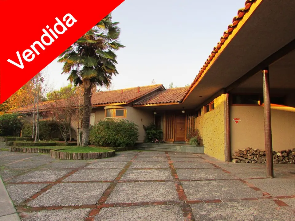 Beige house with a red tile roof and a "Vendida" banner in the upper left corner. A palm tree stands in front of the house.