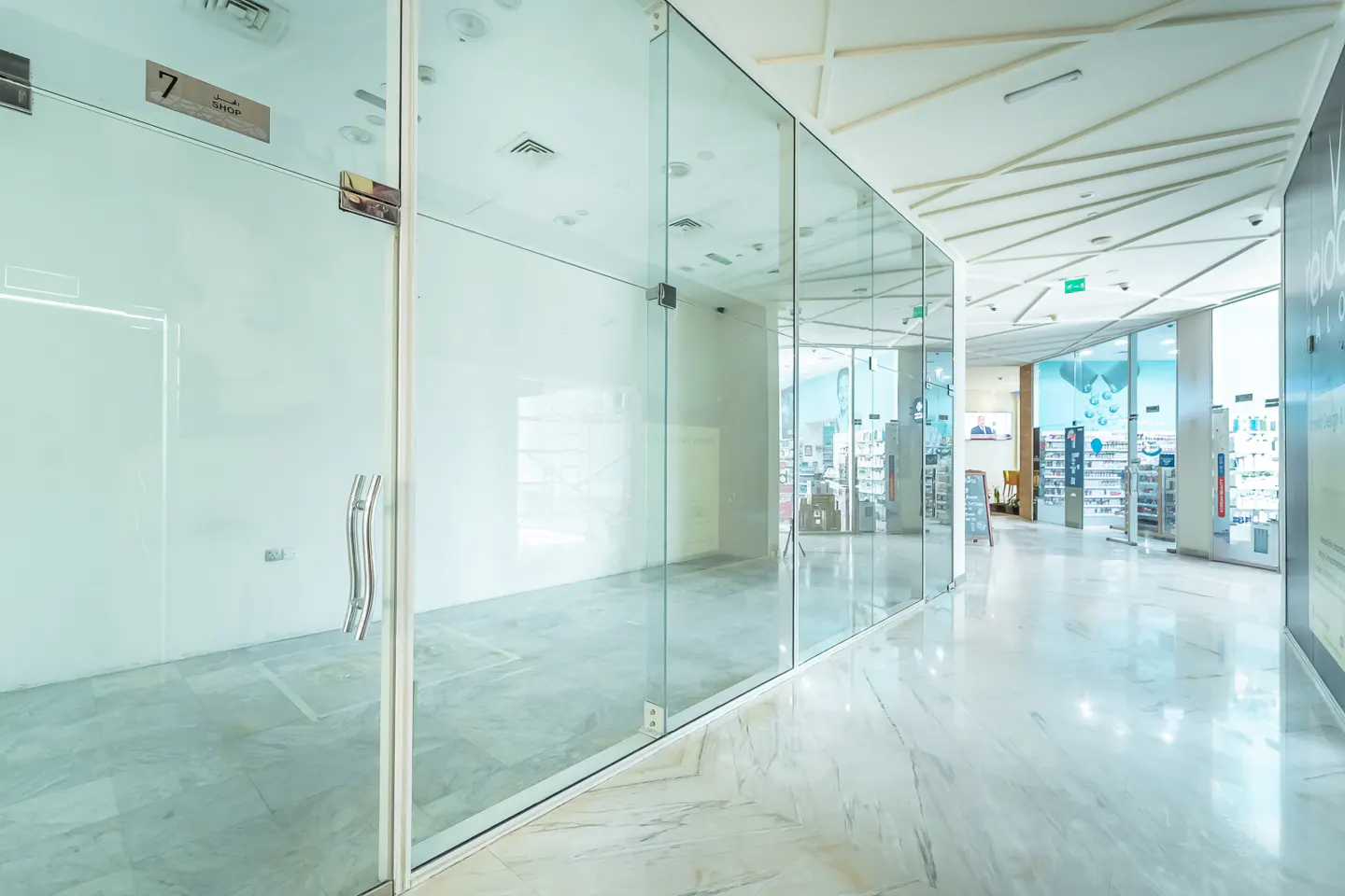 A bright hallway with glass-walled shops and a marble floor.