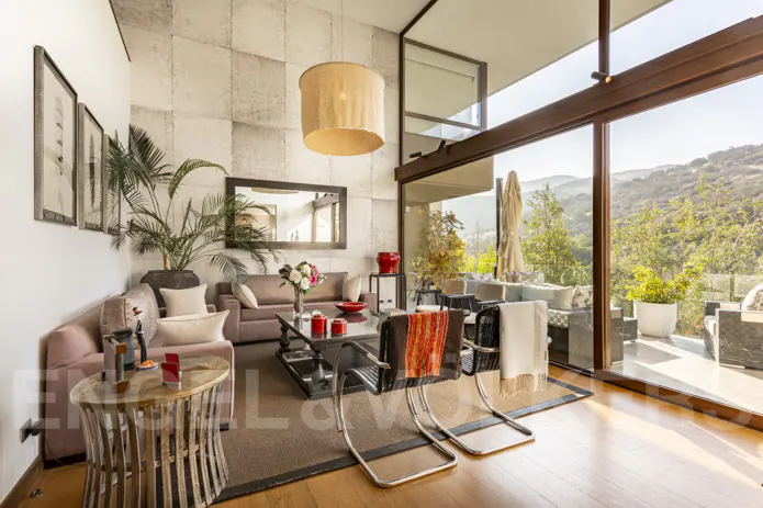 Living room with sofas, chairs, and a view of the mountains through large windows. A tan drum shade hangs from the ceiling.