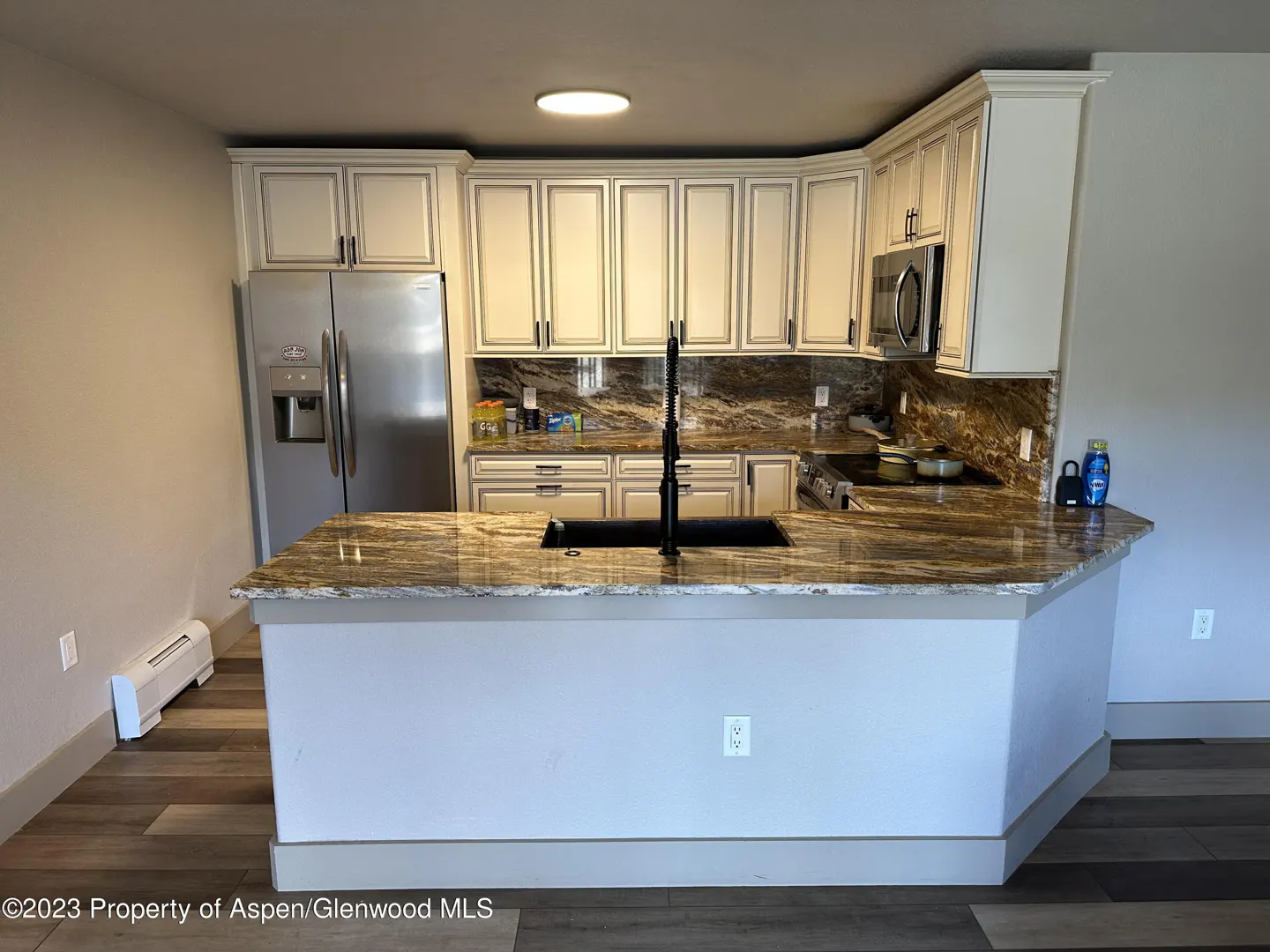 A modern kitchen with white cabinets, granite countertops, stainless steel appliances, and wood floors.