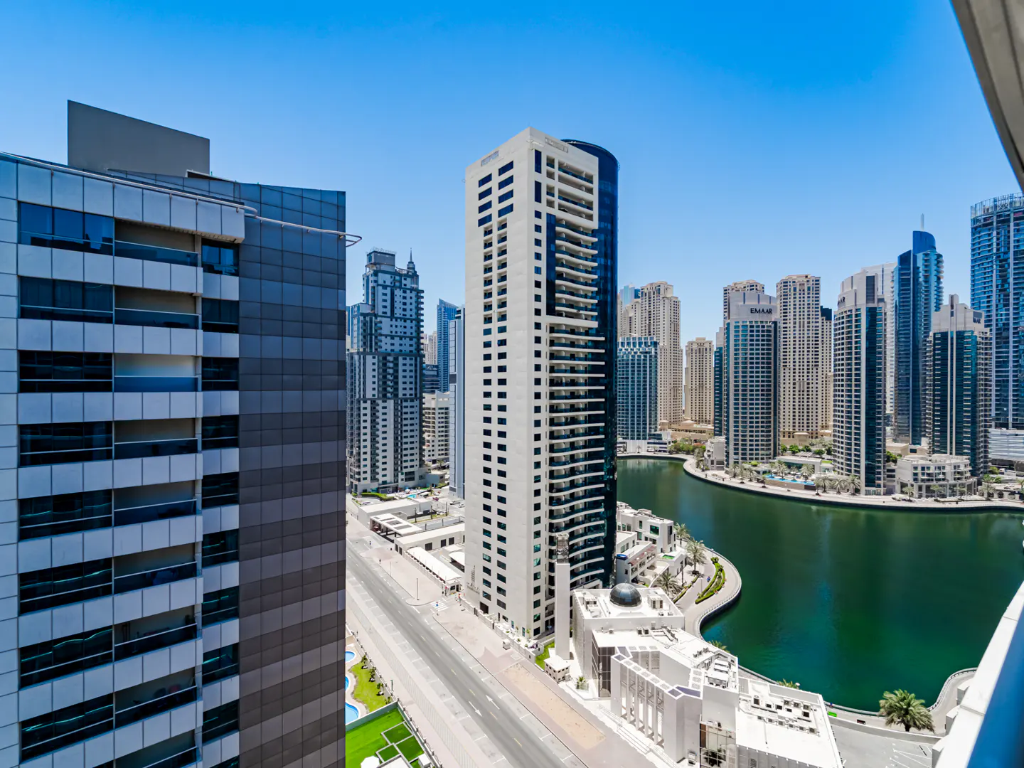 High-angle view of Dubai Marina skyscrapers, a canal, and a street under a clear blue sky.