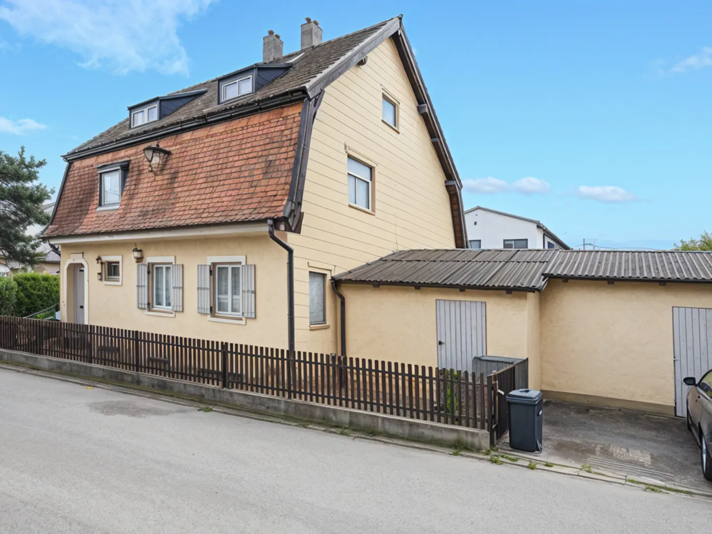 Two-story yellow house with a red tile roof and brown fence under a blue sky.
