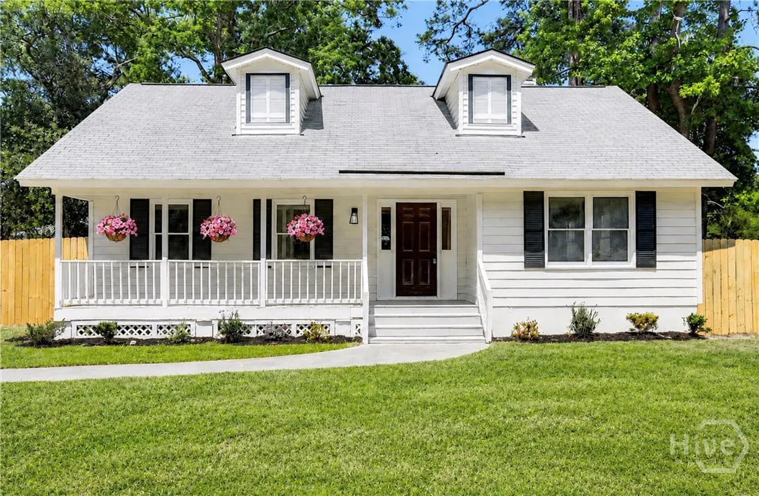 A white, one-story house with a gray roof, black shutters, and a porch with hanging pink flower baskets.