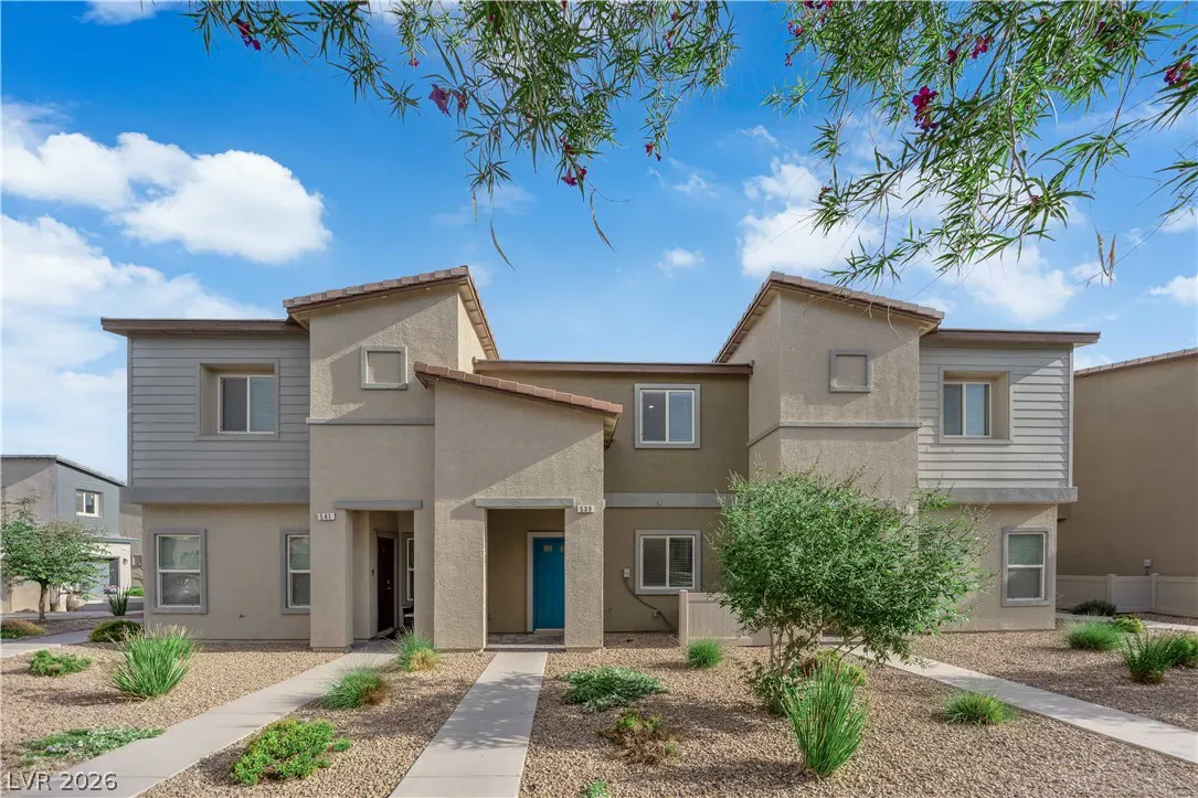 Beige two-story townhouses with blue door and desert landscaping under a blue sky with wispy clouds.