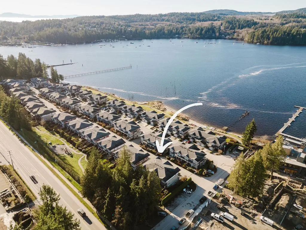 Aerial view of waterfront townhouses with an arrow pointing to one. Blue water and green trees in the background.
