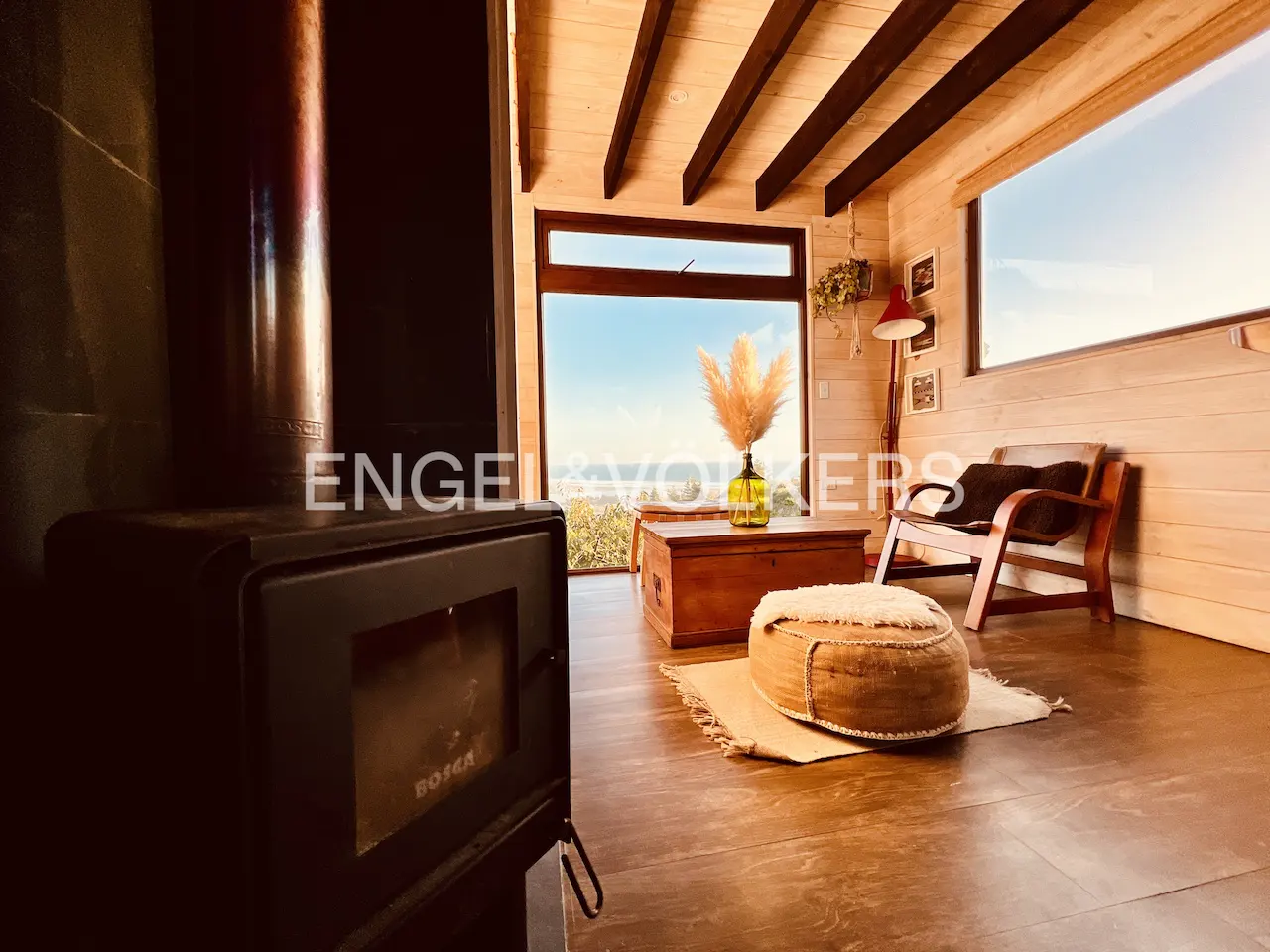 Living room with wood-paneled walls, a black wood-burning stove, and a large window with a view.