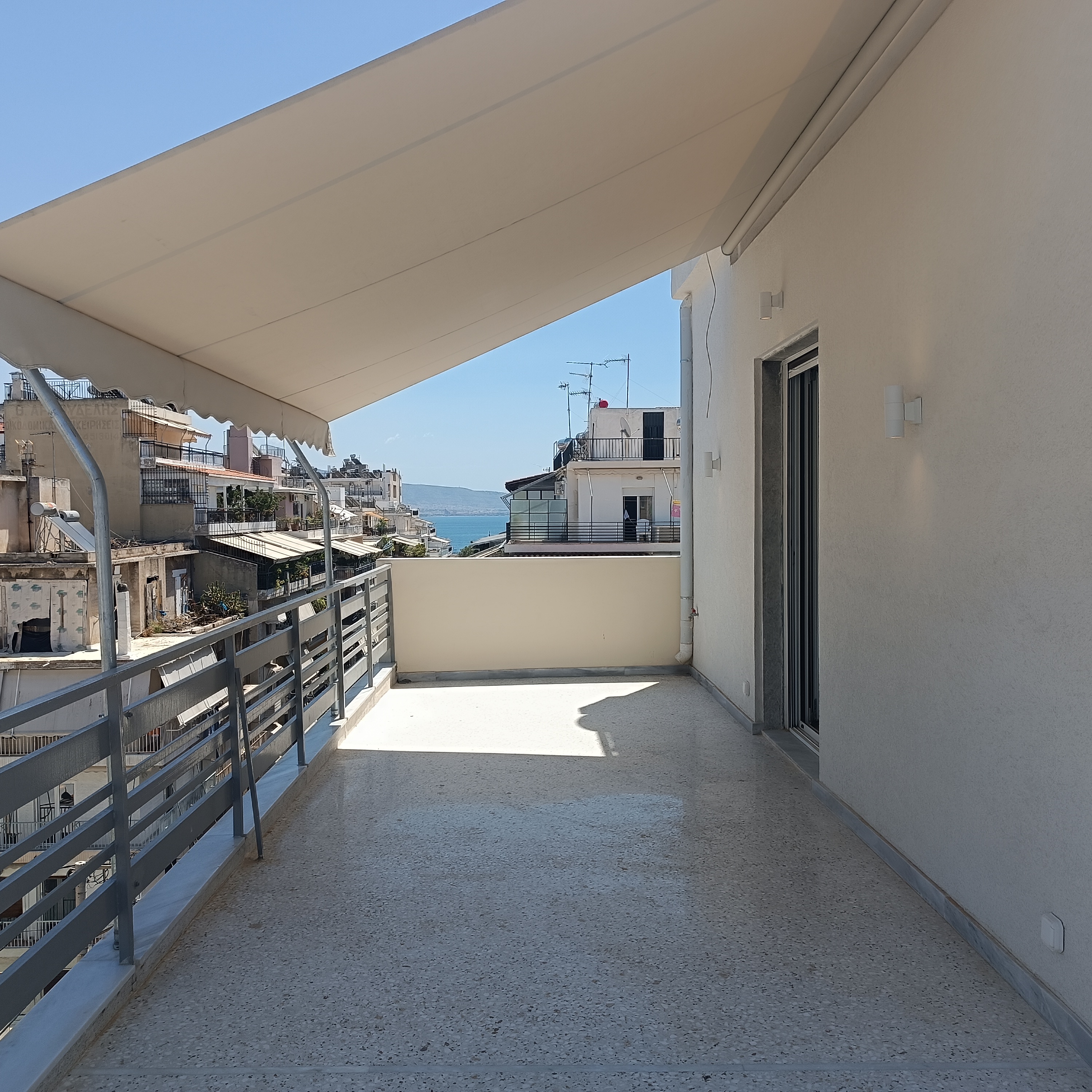 Wide balcony with a retractable awning, metal railings, and a view of the city and sea.