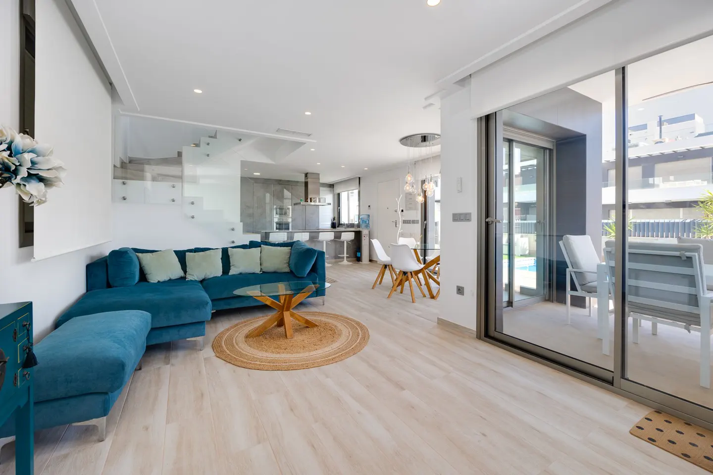 Modern open-plan living room with a blue sectional sofa, glass coffee table, and sliding doors leading to a patio.