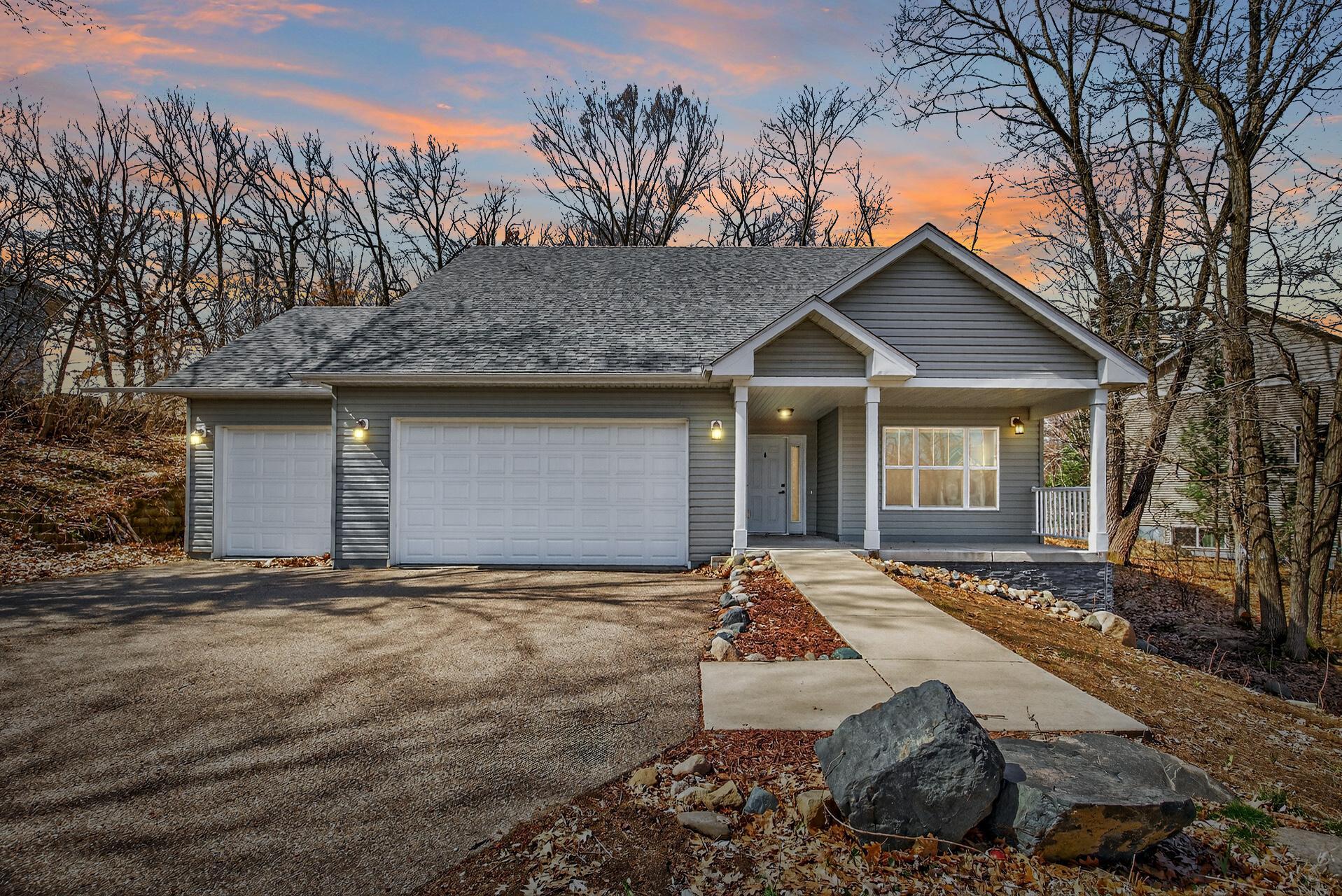 A gray, one-story house with a two-car garage, a walkway, and a sunset sky.