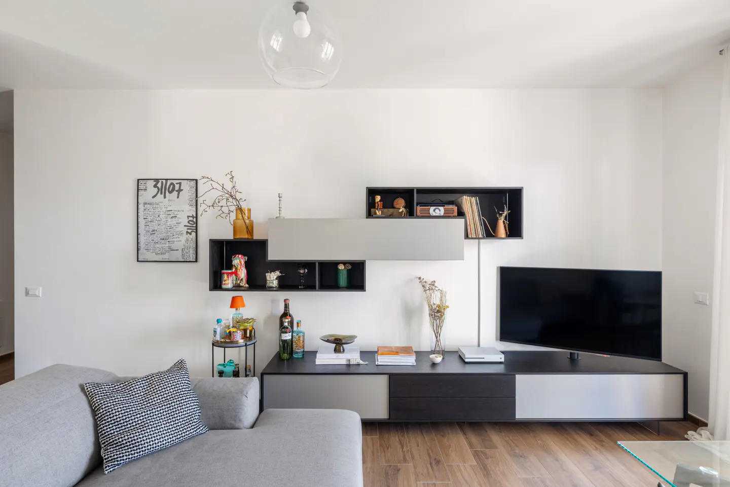 Living room with a gray sofa, a black and gray entertainment center, and a flat-screen TV on a wood floor.