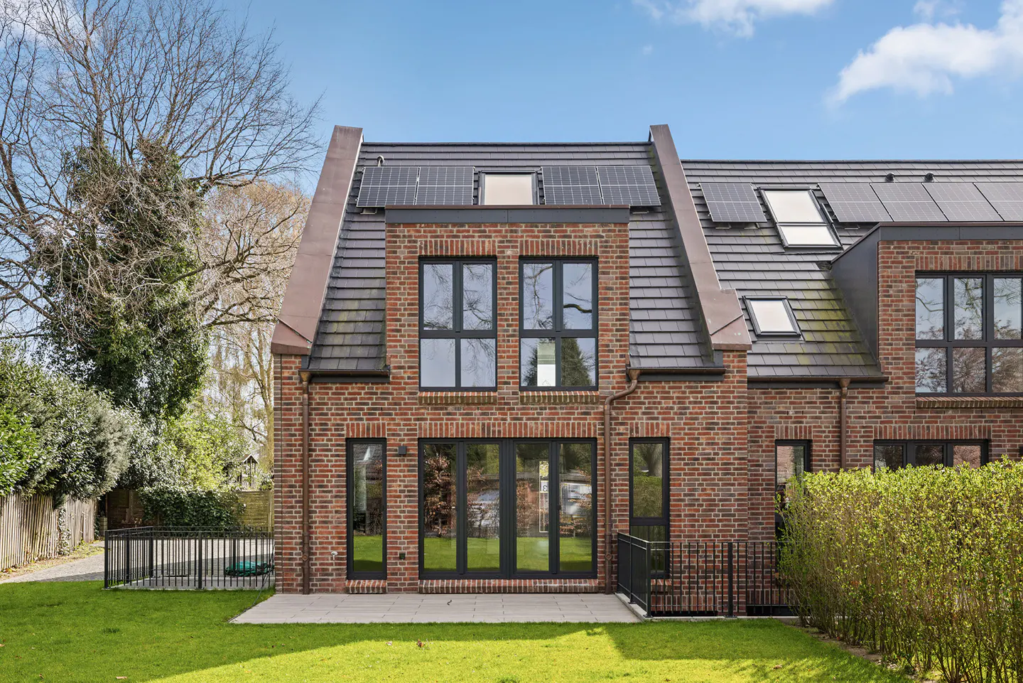 Brick house with black framed windows, a gray roof with solar panels, and a green lawn under a blue sky.