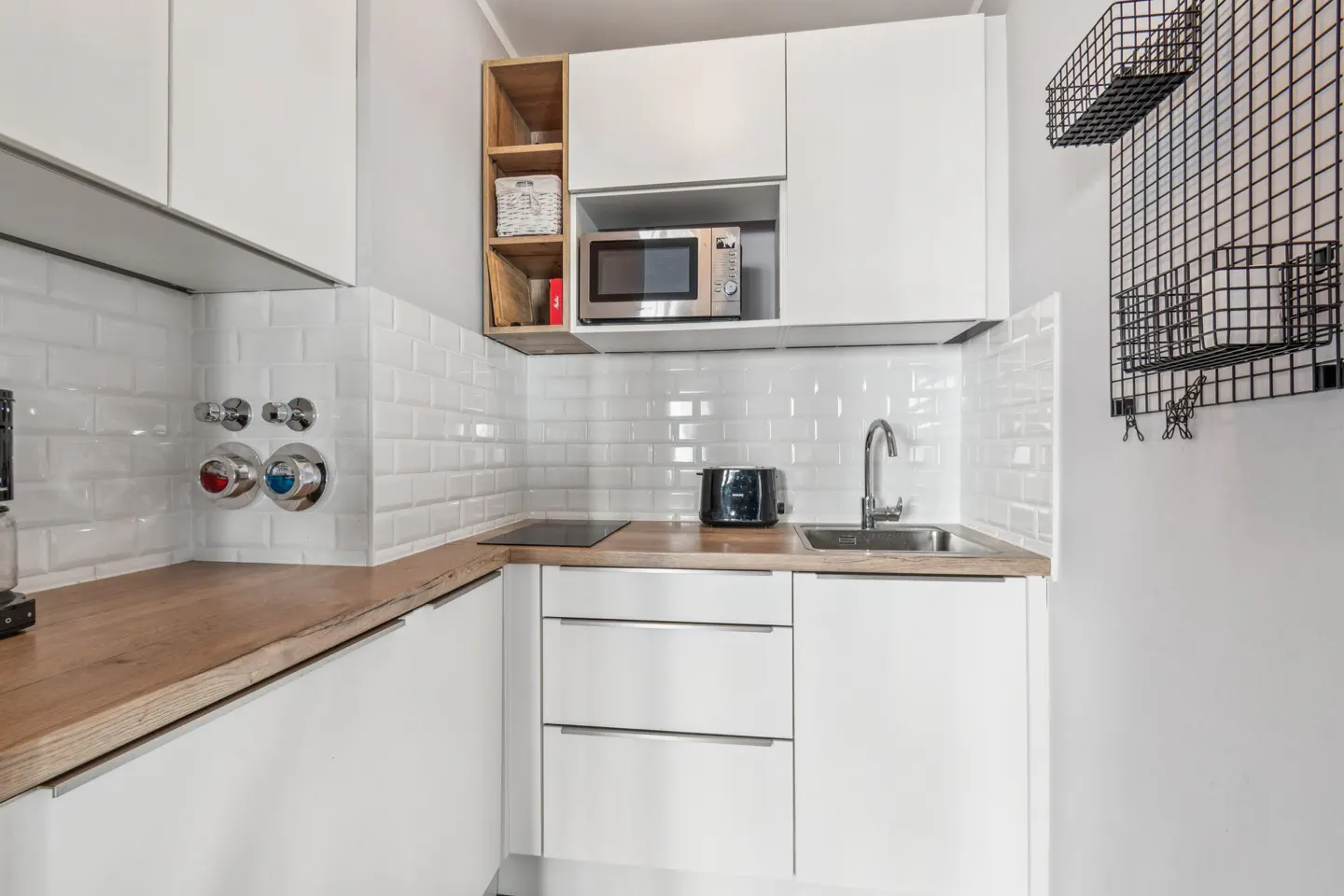 A modern kitchen with white cabinets, subway tile backsplash, and wood countertops. A microwave is built into the upper cabinets.
