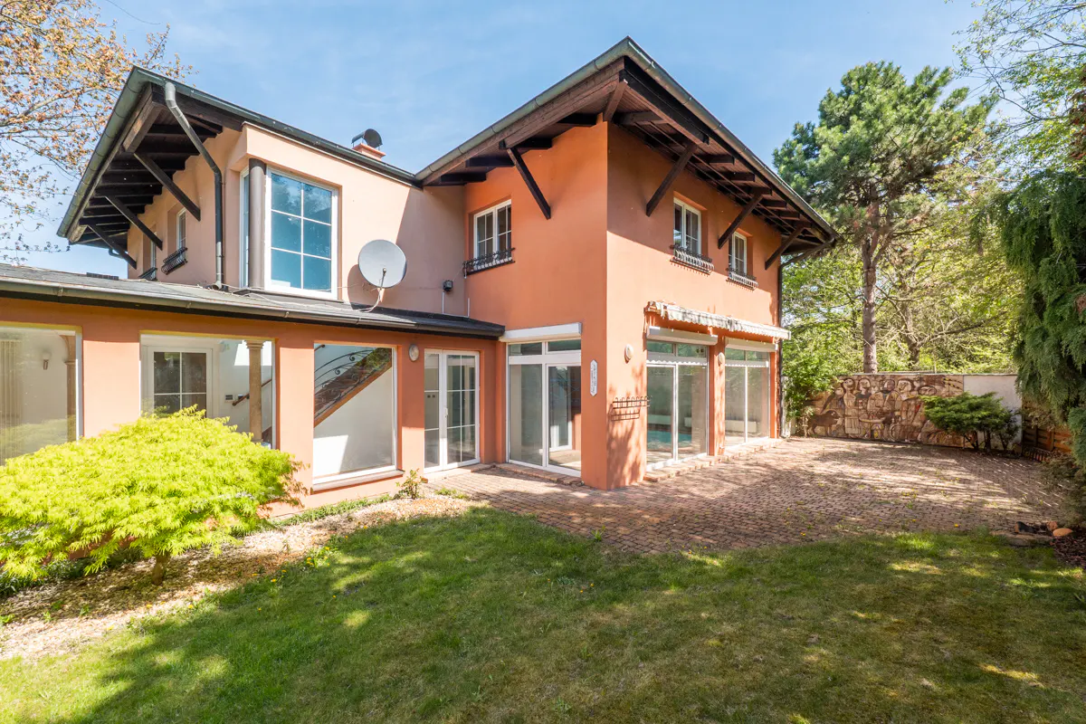 Two-story peach house with white trim, large windows, and a satellite dish. Green lawn and trees surround the property.