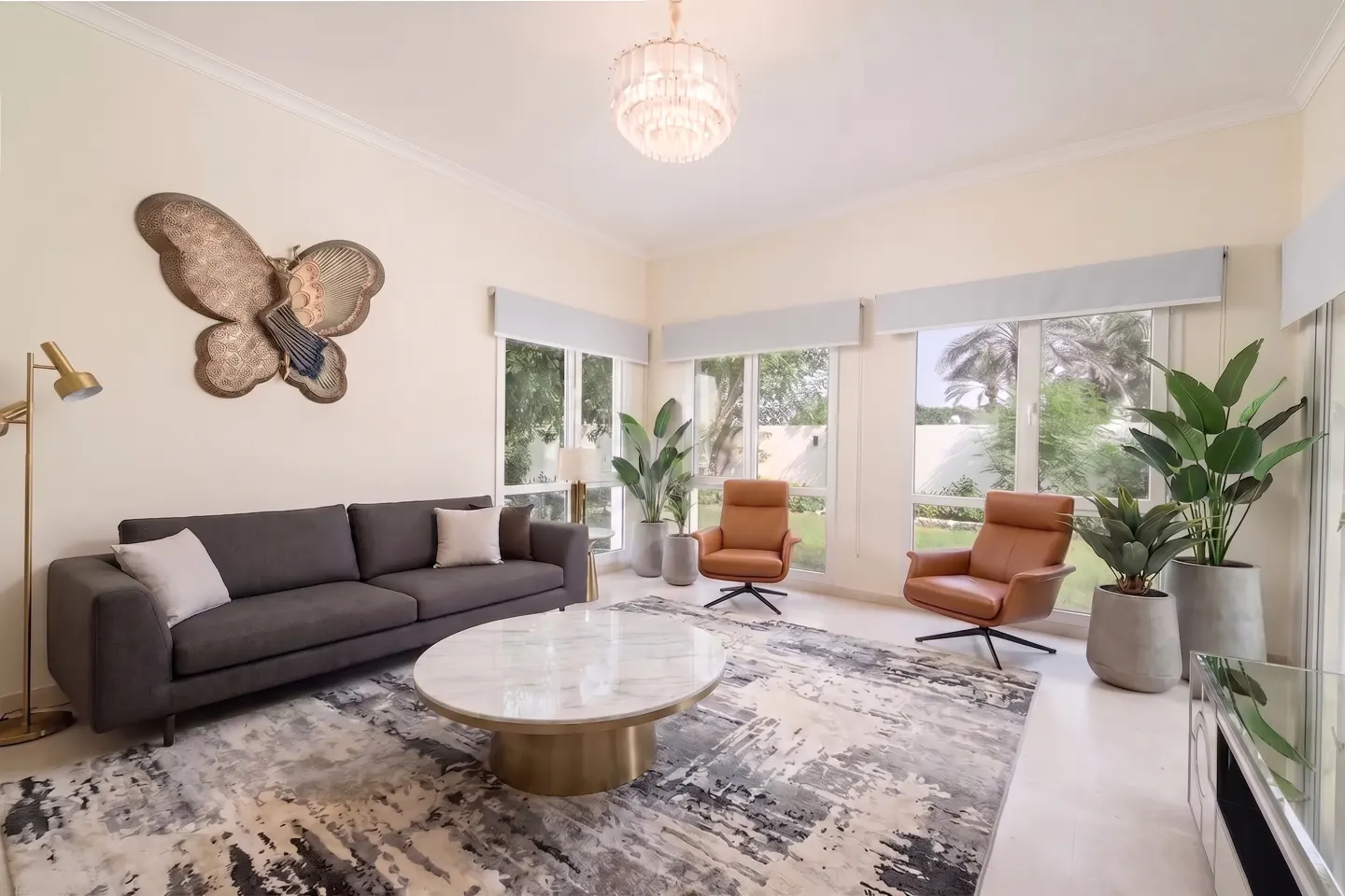 Bright living room with a dark grey sofa, two tan leather armchairs, a marble coffee table, and large butterfly wall art.