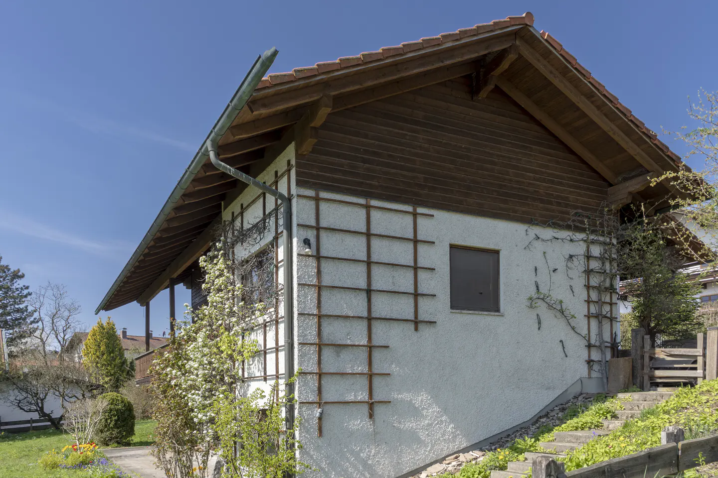 Exterior view of a white stucco house with a brown wood gable and a red tile roof. Trellises adorn the walls.