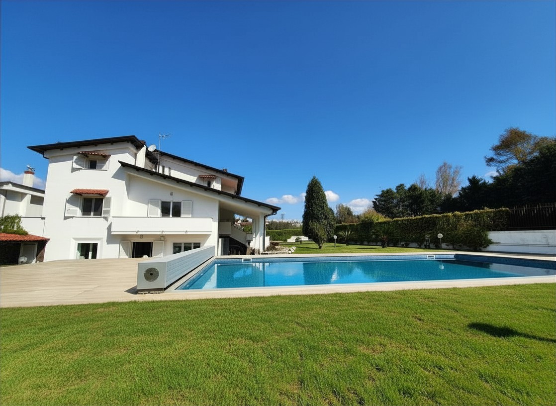 A white two-story house with a blue swimming pool and green lawn under a clear blue sky.