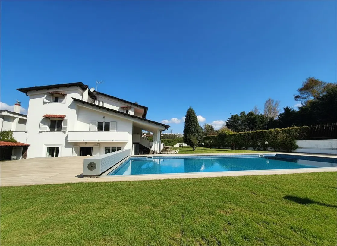 A white two-story house with a blue swimming pool and green lawn under a clear blue sky.