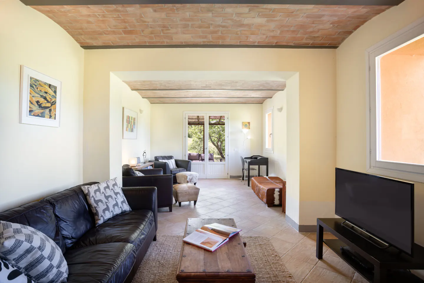 Living room with black leather sofas, a wooden coffee table, brick vaulted ceilings, and glass doors to a garden.