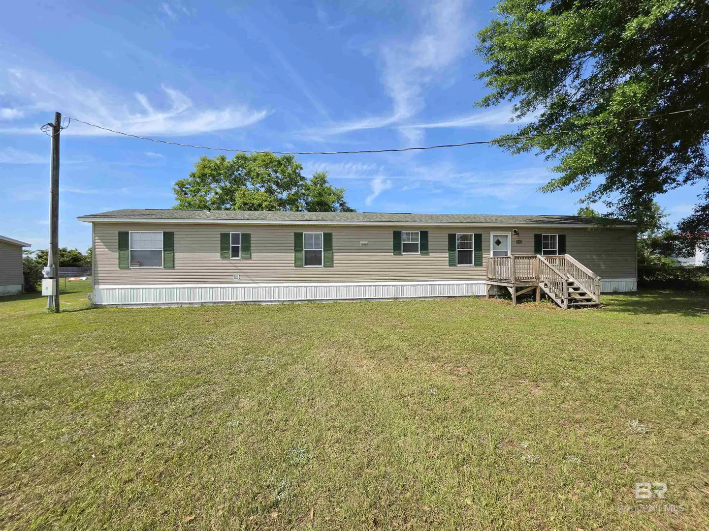 A beige single-story home with green shutters and a small porch, set on a green lawn under a blue sky.