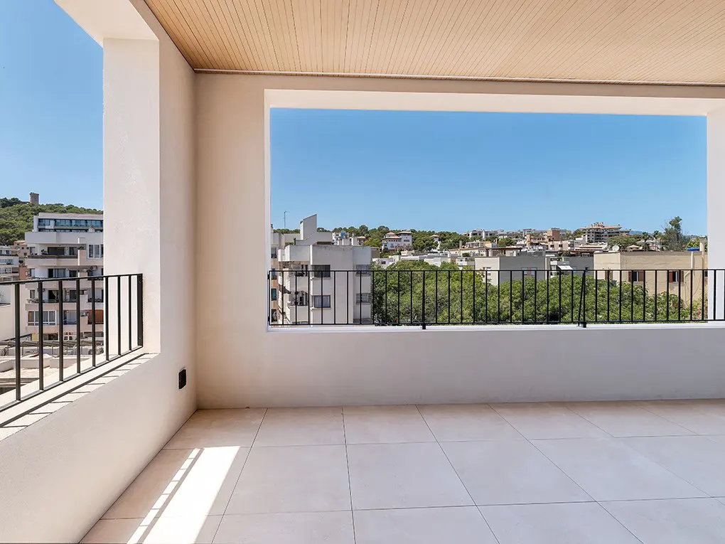 Balcony view with black railings, white tile floor, and city skyline under a blue sky.