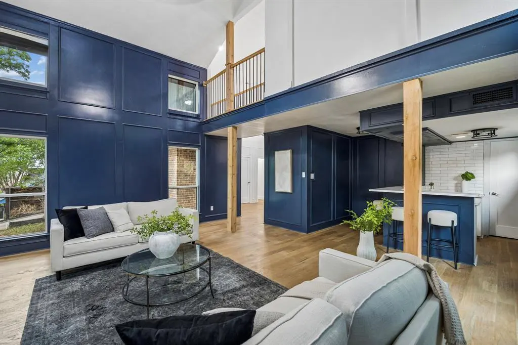 Open-concept living room and kitchen with blue walls, wood floors, and white sofas. A glass coffee table sits on a gray rug.