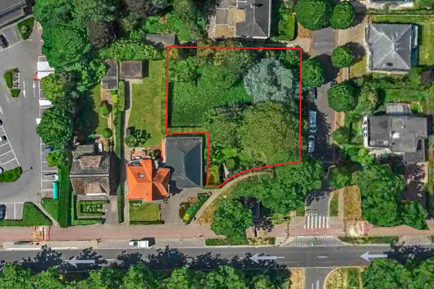 Aerial view of a vacant lot outlined in red, surrounded by trees and houses in a residential area.
