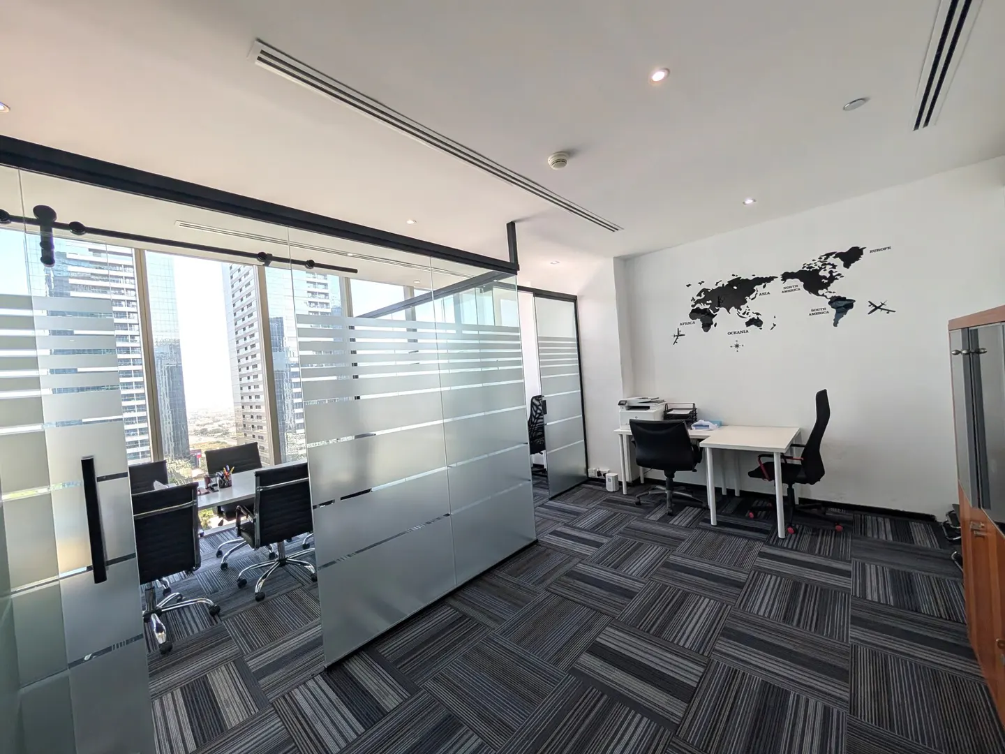 Bright office space with a glass-walled conference room, black chairs, and a world map decal on a white wall.