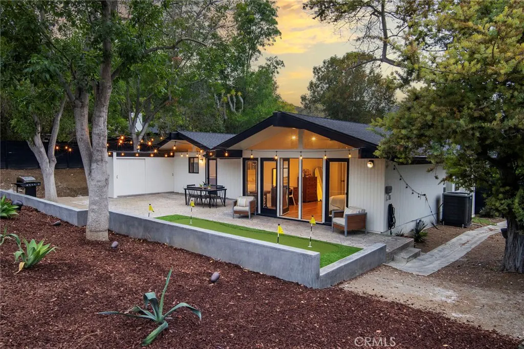 Modern white home with a backyard putting green, patio seating, and string lights at sunset.