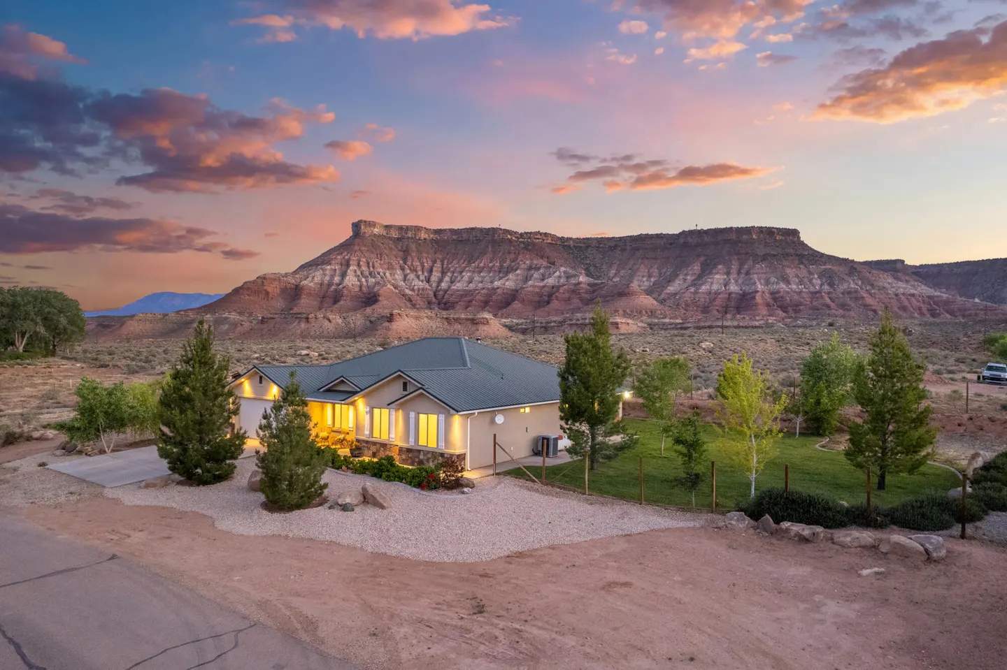 A tan house with a green roof sits before a red rock mountain at sunset.