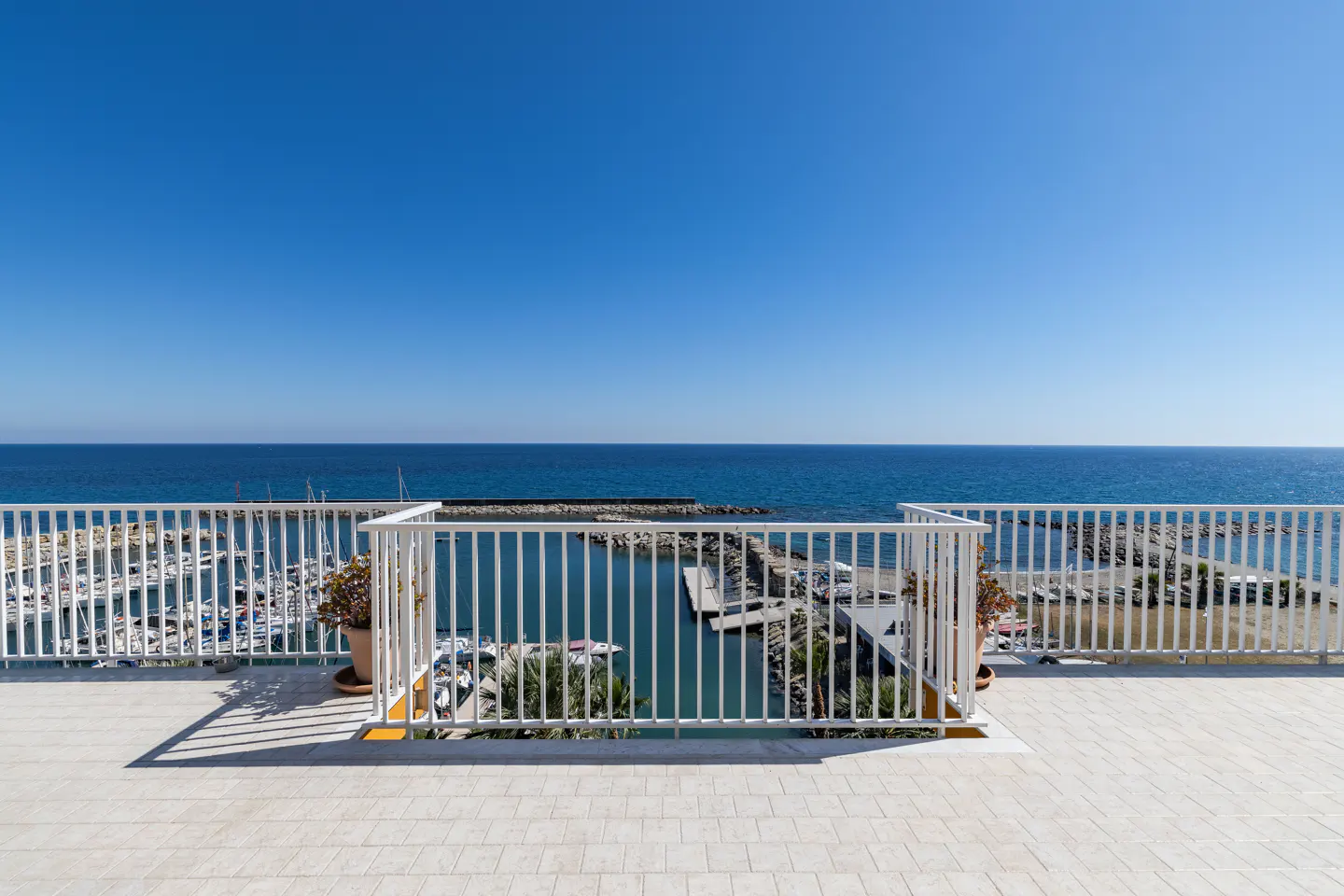 Balcony view of a marina with boats, white railings, and a blue sky.