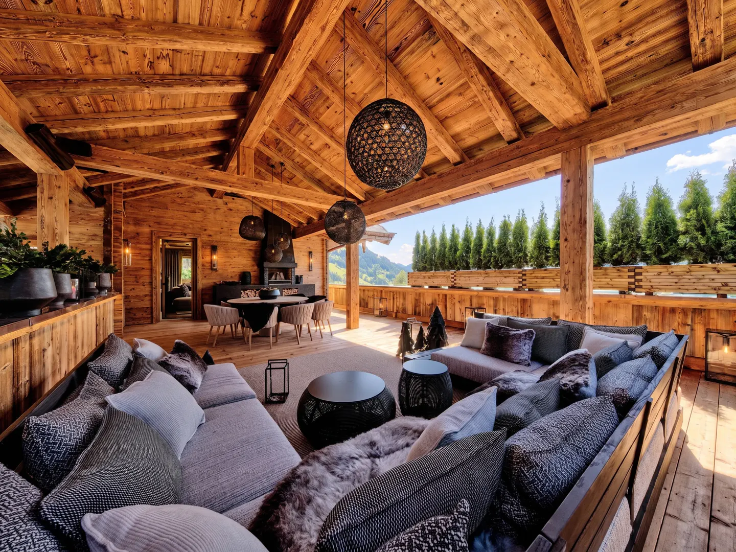 A rustic, wood-paneled chalet interior with a large sofa, dining table, and mountain view.
