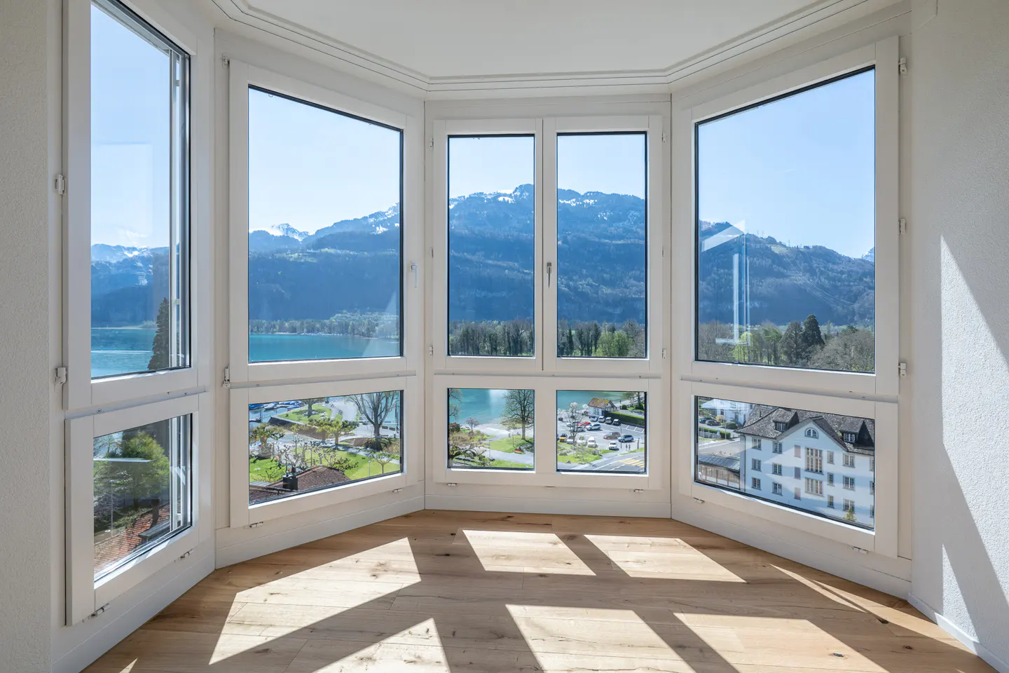 Bright room with bay windows overlooking a lake and mountains. Light wood floors and white trim.
