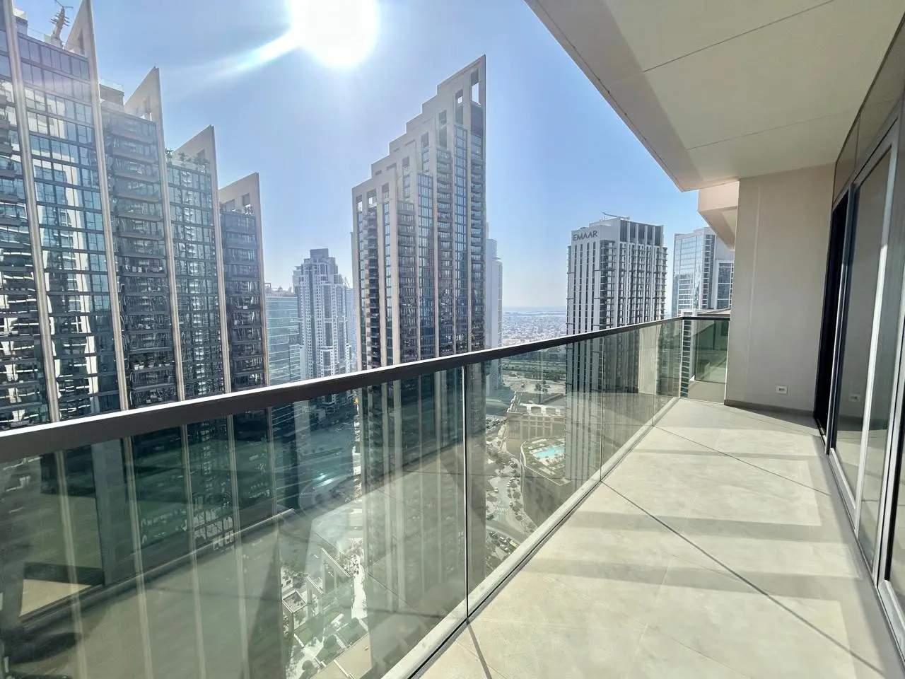 View from a high-rise balcony with glass railings, overlooking a city skyline under a bright, sunny sky.