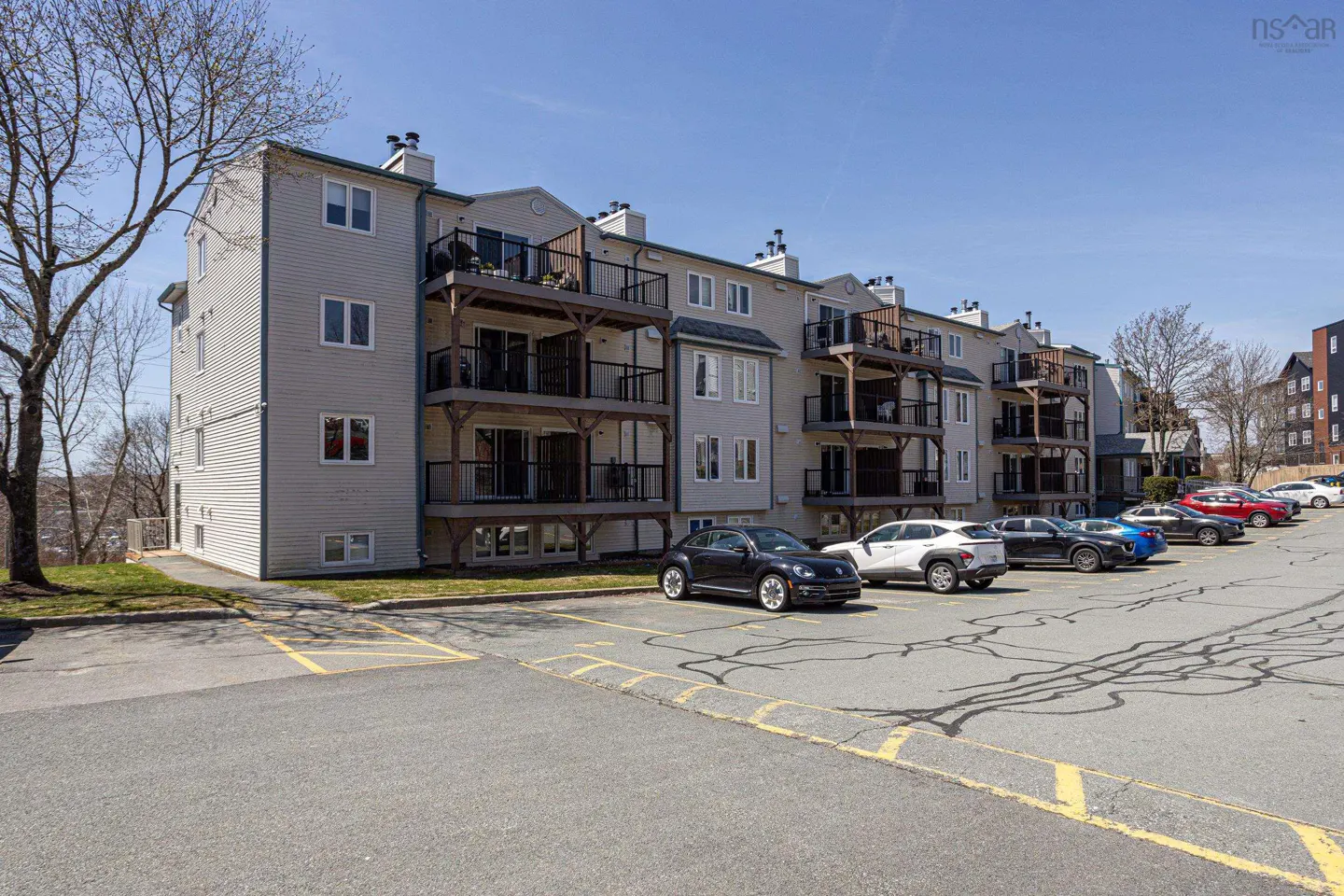 A three-story apartment building with balconies and a parking lot in front.