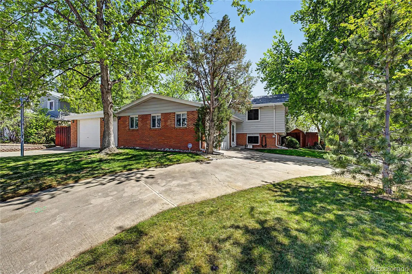 Two-story house with brick and light gray siding, a concrete driveway, and green trees.