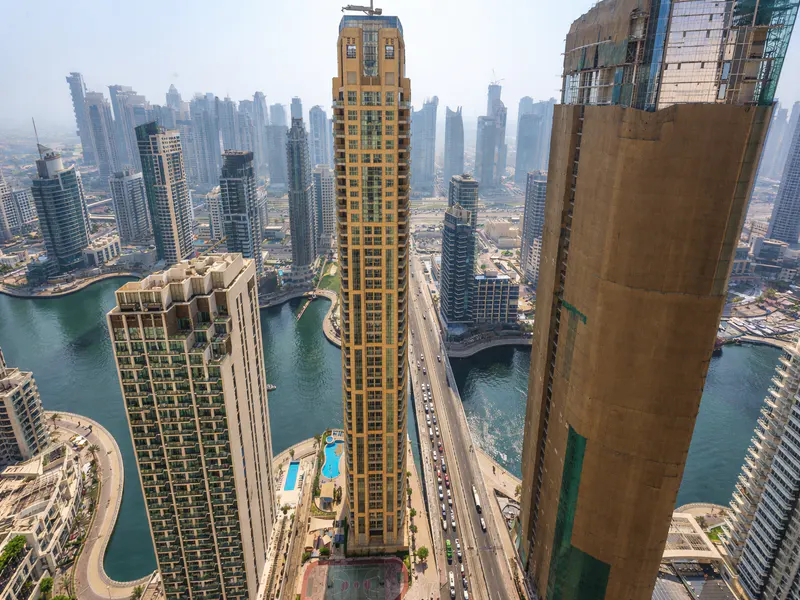 Aerial view of Dubai Marina with skyscrapers, a bridge with traffic, and a blue swimming pool.