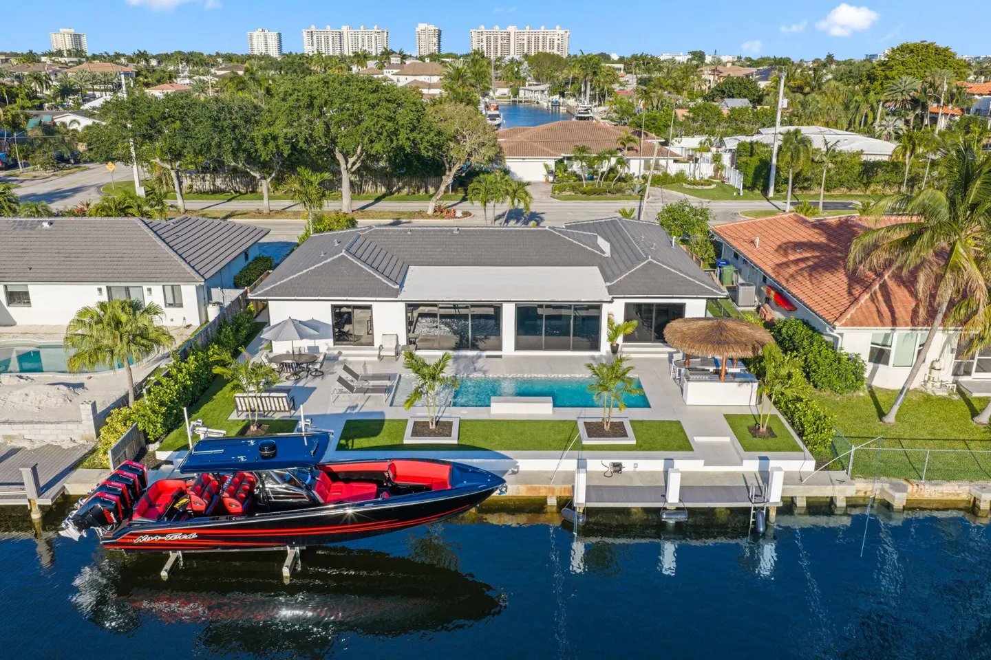 Aerial view of a modern white waterfront home with a pool and a black and red speedboat docked.