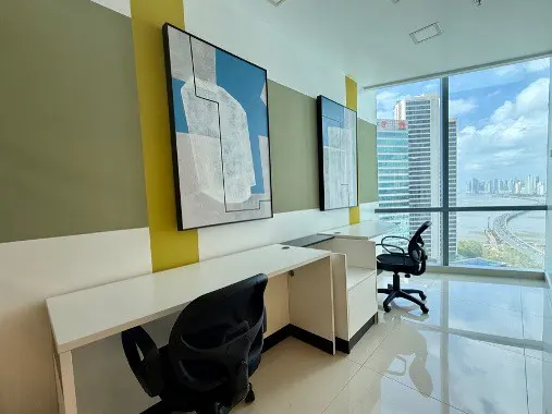 Bright office space with white desks, black chairs, and abstract art. Large windows offer a city and ocean view.