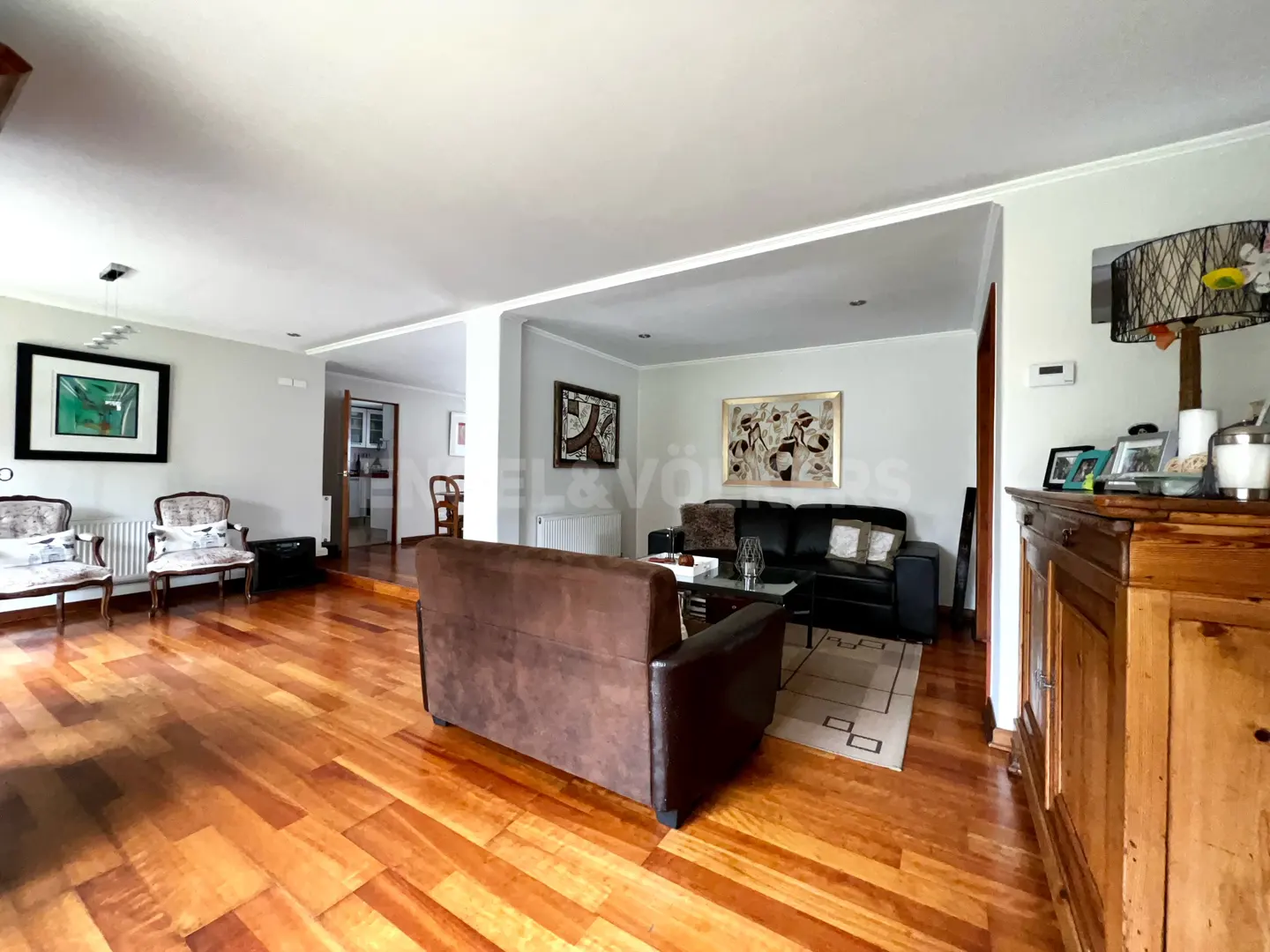 Spacious living room with hardwood floors, a brown sofa, black leather seating, and a wooden cabinet with a lamp.