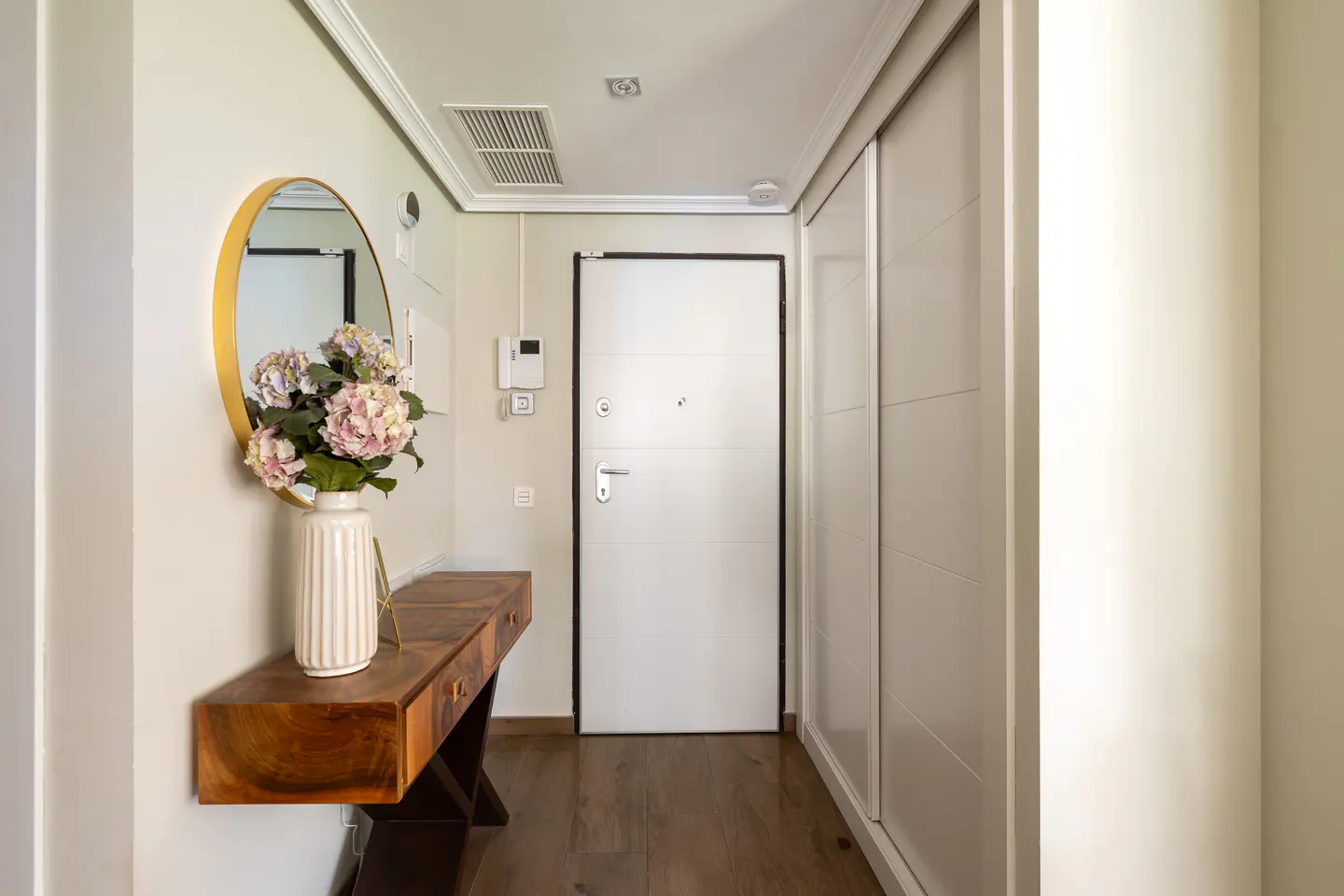Entryway with wood floors, a white door, and a wood console table with flowers and a gold mirror.