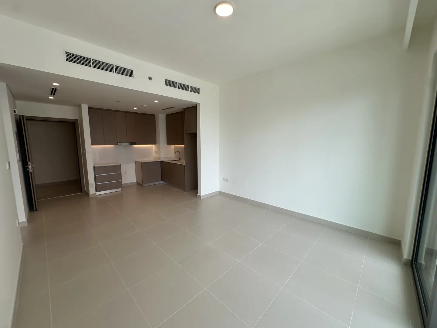 An empty apartment with gray tile floors, white walls, and brown kitchen cabinets.