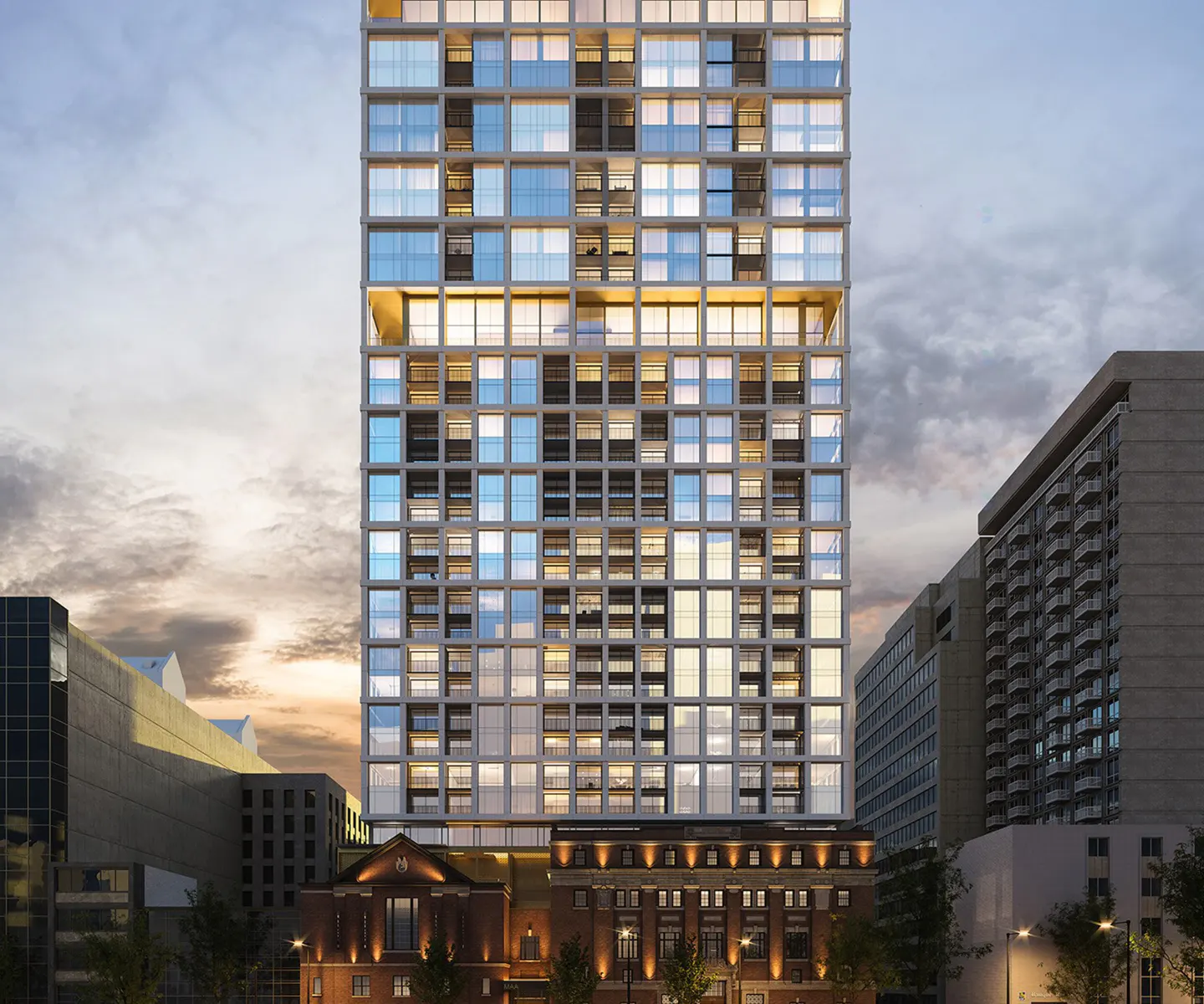Modern high-rise building with a grid of windows, atop a brick building, against a dusk sky.